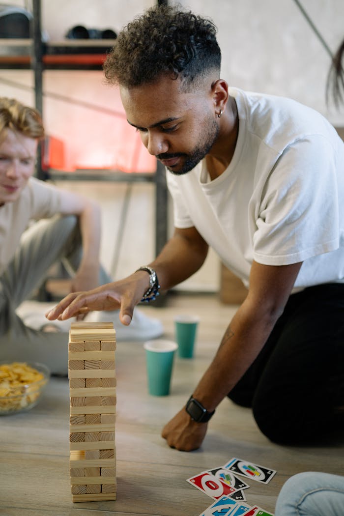 Focused man carefully playing Jenga at game night, surrounded by friends and fun.